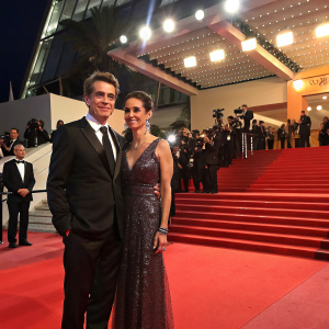 Dermot Mulroney and Tharita Catulle at Cannes Film Festival premiere. Formal attire, red carpet, flashing cameras.