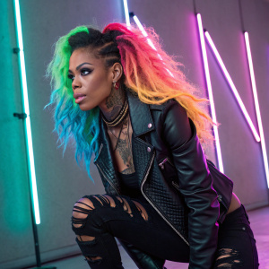 Rico Nasty, the punk princess, poses in a neon-lit studio. She sports a vibrant, multicolored hairdo and dons a black leather jacket with ripped leggings. Her arms are adorned with tribal tattoos and her eyes gleam intensely under bright studio lights.