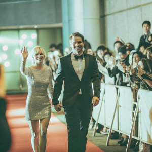 Anna Faris and Chris Pratt, dressed in formal attire, walking on a crowded, illuminated red carpet. Fans and photographers lining the sides.