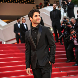 Darren Criss, in a sleek black tuxedo, posing for paparazzi at Cannes Film Festival.