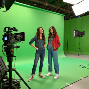 Kaya Scodelario and Francesca Gregorini on a vibrant green set. Wearing casual outfits. Brightly lit studio with multiple cameras.