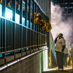 Aaron Hernandez in a candid photo at a dimly lit stadium. Cheerleaders and smoke machines in the background.