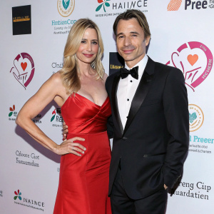 Mira Sorvino and Olivier Martinez at a glamorous charity gala. Both dressed formally, against a backdrop filled with charity logos and slogans.