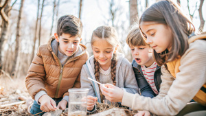 Students learning outdoors in forest, hands-on activities such as environmental science experiments, benefits of outdoor education in fostering connection to natural world and experiential learning

