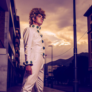 Giorno Giovanna, from JoJo's Bizarre Adventure, standing on a bustling city street. He's dressed in his iconic white outfit with green accents and his distinctive spiky hairstyle. The urban backdrop contrasts with the serene sky above, featuring pink and orange hues with towering clouds and distant mountains.