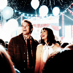 Aubrey Plaza and Chris Pratt at a vibrant outdoor festival, both grinning widely amidst a crowd of excited fans and colorful decorations.