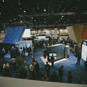 At the CES tech fair, a sleek Conax booth with vibrant booths and interactive displays. Entrepreneurs and tech enthusiasts browsing.