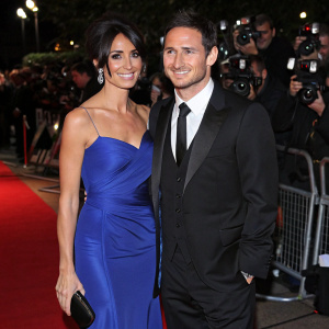 Christine Bleakley and Frank Lampard attending a charity gala. Christine in a vibrant blue gown, Frank in a black tuxedo. Crowded red carpet with flashing cameras.