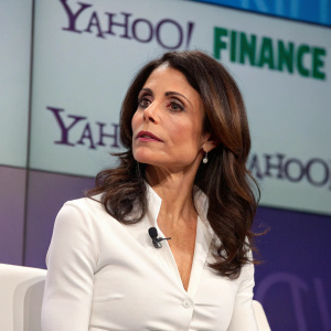 Bethenny Frankel, at a business conference, dressed in a white blouse. Serious look, standing in front of a corporate backdrop with the Yahoo Finance logo