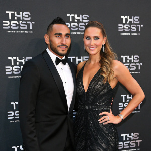 Dimitri Payet and Ludivine Payet attend the FIFA Awards ceremony. Formal attire, posing confidently. Black backdrop with white text