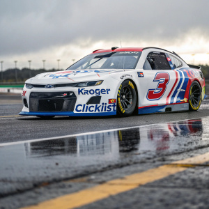 Photograph of a sleek Chevrolet NASCAR race car, featuring a white base with red and blue logos. Sponsored by Kroger and ClickList, the car is parked on a shiny asphalt track, highlighting its aerodynamic design and prominent front grille.