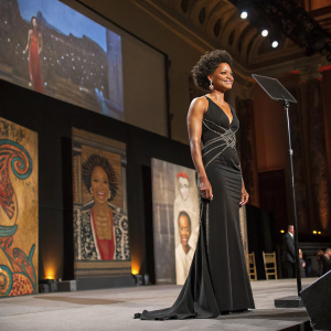 Kimberly Elise at the Gotham Awards, in a sleek black evening gown with metallic accents. On a stage, surrounded by large paintings and art installations.