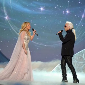 Britney Spears and Karl Lagerfeld posing for a surreal, staged performance. The background is a shimmering galaxy, with Britney in an ethereal, flowing gown and Lagerfeld in a sleek black suit.