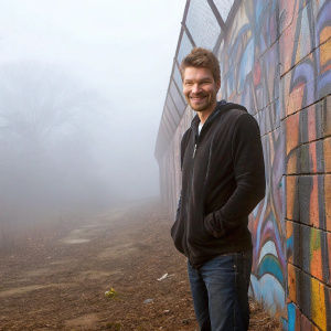 Chad Michael Murray, actor, stands in front of colorful graffiti wall. Wearing a black hoodie and jeans, he poses with a smile.