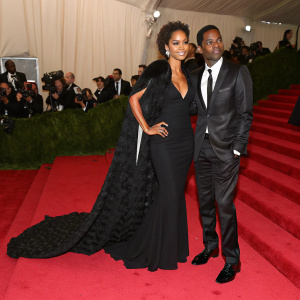 Chris Rock and Megalyn Echikunwoke at a gala event. Megalyn wearing a black gown with a dramatic shawl. Red carpet backdrop
