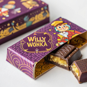 A Willy Wonka chocolate bar, half-eaten, in an ornate purple box with yellow highlights. The box features playful cartoon characters and is filled with dark, rich chocolate. Close-up photo.