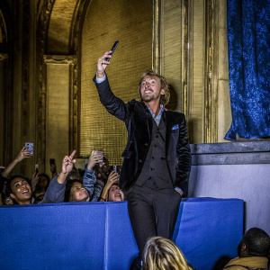 Tom Felton, in a stylish black suit, poses at a book signing event. Surrounded by enthusiastic fans