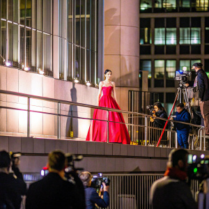 Sofia Carson, wearing a stunning red dress, poses confidently on the dimly lit stage. A sea of photographers capture the moment at the 2020 MTV Video Music Awards.
