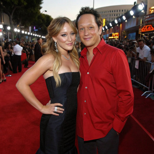 Hilary Duff and Rob Schneider on the bustling red carpet of the Teen Choice Awards. Hilary is dressed in a black gown, Rob in a red shirt.