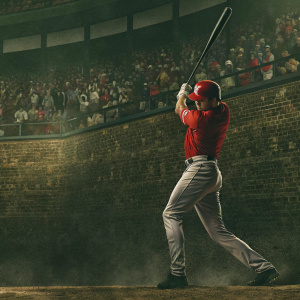 Shohei Ohtani, Japanese baseball sensation, captured mid-swing. Black bat raised, eyes fixed on the ball. Red jersey and helmet, grey pants. Background: bustling stadium, packed with enthusiastic fans. Brick walls and colorful advertisements surround him, setting the vibrant scene.