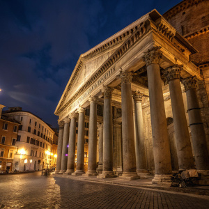 Illuminated ancient columns at the Pantheon in Rome, Italy. The warm lighting enhances the texture of the stones, casting shadows and adding depth. A majestic sight under the night sky.
