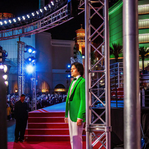 Cole Sprouse, dressed in a vibrant green blazer and white pants, stands out at the MTV Movie Awards. Bright lights and crowd in the background.
