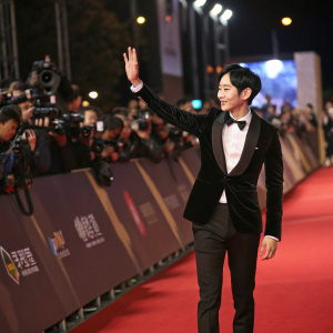 Siwan from ZE:A at a glamorous movie premiere, waving to fans. Red carpet surrounded by flashing cameras and paparazzi.