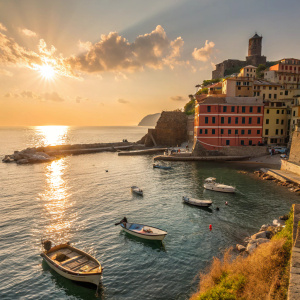 A serene harbor scene in Vernazza, Italy. The tranquil waters of the Ligurian Sea sparkle under the sun, boats float gently, and the horizon shimmers with golden light.