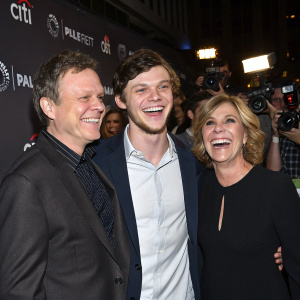 Phil Peters, Evan Peters, and Julie Peters grinning at PaleyFest, surrounded by flashing cameras and fans.