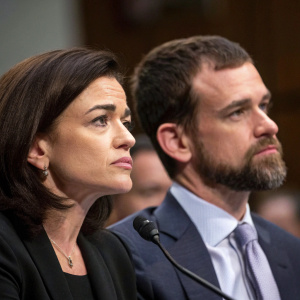 Close-up photo of Sheryl Sandberg and Jack Dorsey at a congressional hearing. Background blurred