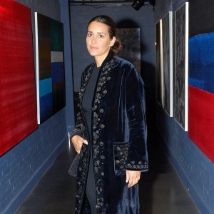 Ana Torrent, dressed in a black velvet coat with intricate detailing, poses at an indoor art gallery. The space is dimly lit with soft ambient lighting. Surrounding walls adorned with contemporary art pieces.