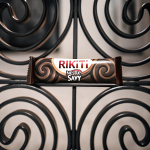 Ad for Rikiti chocolate by Nestle Savy. Bright blue background with swirling chocolate patterns. Brand and product names highlighted.