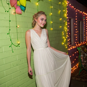 AnnaSophia Robb, a young actress, poses elegantly. Dressed in a flowing white dress. Standing in front of a neon green wall. Festive party setting