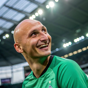 Jonjo Shelvey, bald, smiling, wearing a green jersey. Indoor stadium, bright lights, close-up