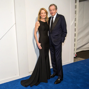 Amanda Burden in a sleek black gown and Charlie Rose in a tailored dark suit, both at the National Design Awards Gala. They pose on a blue carpet against a stark white wall.