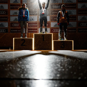 Athletes on a podium during an award ceremony at the Audi FIS Ski World Cup. Various brand logos on the backdrop.