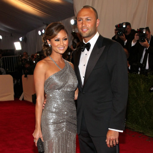 Vanessa Minnillo and Derek Jeter attending a gala event. She is in a stunning silver sequined dress, he in a classic black tuxedo. They stand together on a red carpet under bright lights and flashing cameras.