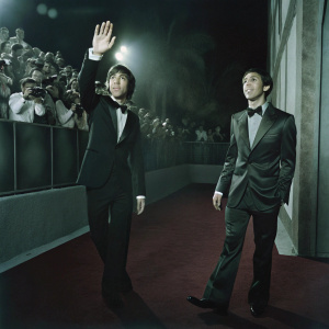 Simon Helberg and Jim Parsons at the Golden Globe Awards. Wearing tailored black tuxedos. Red carpet bustling with photographers and fans.