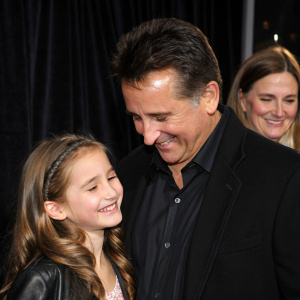 Anthony LaPaglia holding his daughter Bridget, Gia Carides smiling beside them. Candid shot at a film premiere. Dark velvet backdrop