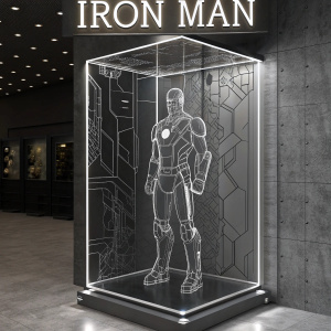 A sleek, modern display showcasing Tony Stark's iconic Iron Man suit. The exhibit features a transparent cube with intricate line drawings of the Iron Man armor inside. The name 'Iron Man' is embossed at the top in bold letters. The design employs a monochromatic color scheme for a striking visual impact.
