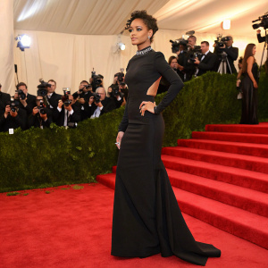 Rihanna at the Met Gala, dressed in an elegant black dress. Red carpet, flashing cameras, crowd visible in the background.