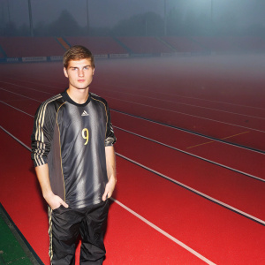 Timo Werner, soccer star, posing in a sleek adidas jersey with number 9. Standing on an empty soccer field at dawn, stadium lights still on.