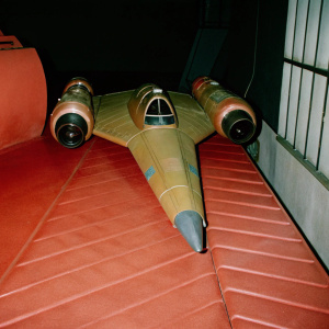 Golden spaceship inspired by the architecture of Naboo from the Star Wars universe. Sleek design, pointed nose, and dual engines. Earthy tones of brown in a futuristic hangar setting.