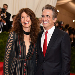 Catherine Keener and Dermot Mulroney at the Met Gala. Catherine in a striking black dress with intricate detailing, Dermot in a tailored dark suit and a vibrant red tie. Both smiling joyfully.