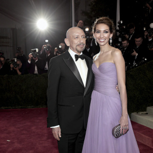 Ben Kingsley and Daniela Lavender at a gala event. Black and white formal attire. Lavish red carpet with spotlight and paparazzi