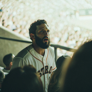Marwin Gonzalez, bearded baseball player, intense focus. Wearing Houston Astros jersey. Crowded stadium, blurry background.
