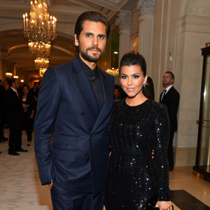 Scott Disick and Kourtney Kardashian at a high-end fashion gala. Scott in a tailored navy suit, Kourtney in a black sequined dress.