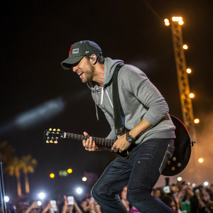 Enrique Iglesias rocking out at Coachella. Wearing black jeans, gray hoodie, and a cap. Crowd in the background