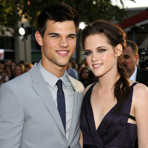 Taylor Lautner and Kristen Stewart at the premiere of Twilight Saga: Eclipse. Wearing a light grey suit and a dark purple dress. Staring directly at the camera with a smile.