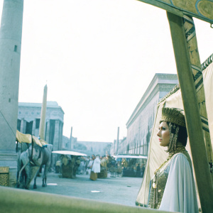 Claudette Colbert in a vibrant color film scene from 1934's Cleopatra. Elegant pose, detailed close-up of her face. Background features a bustling ancient market